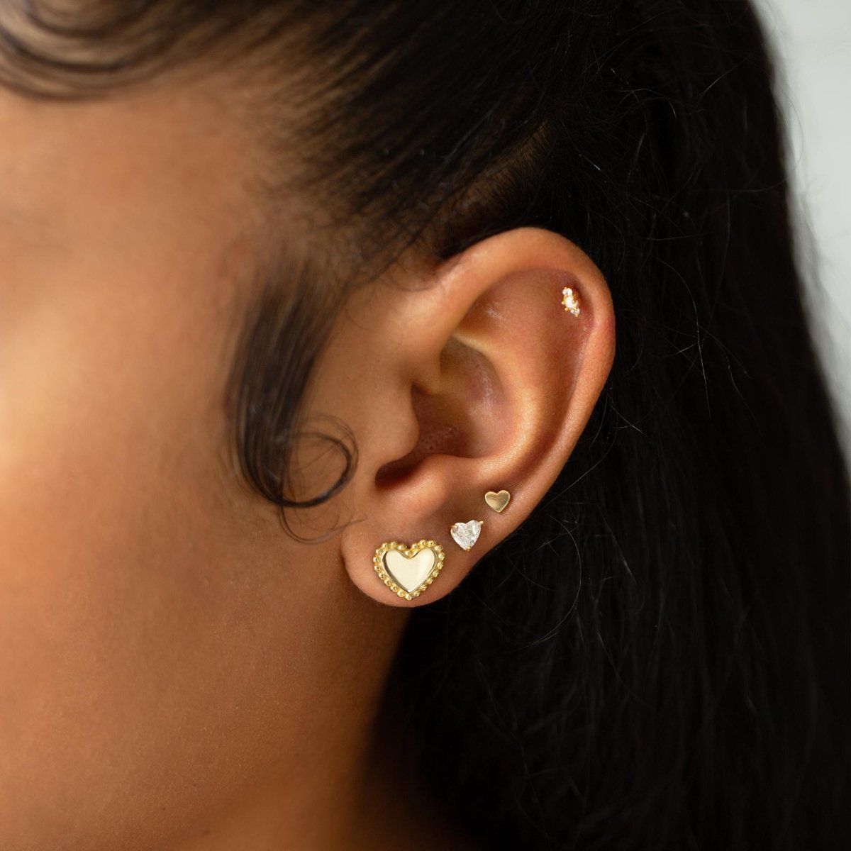 Gold vermeil beaded heart stud shown on a model's earlobe in a multi-piercing stack