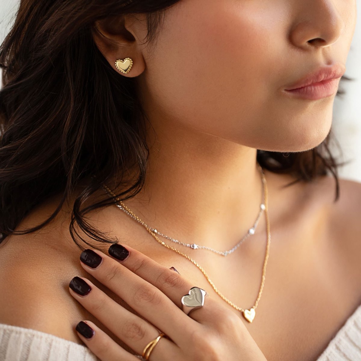 Gold vermeil beaded heart stud shown on a model's earlobe with layered necklaces and ring