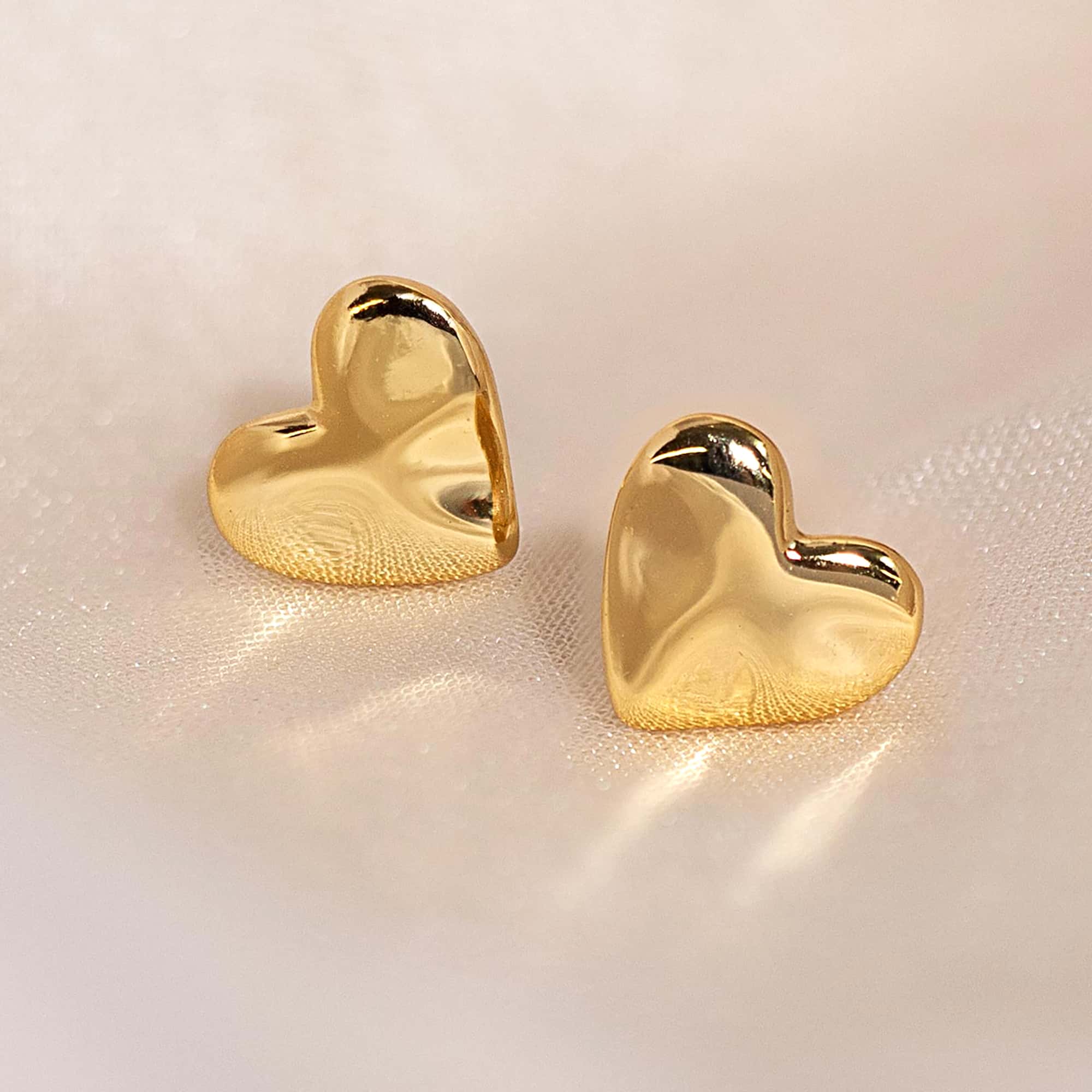 Gold vermeil puffed heart stud earrings with a smooth high-shine finish, on a cream background