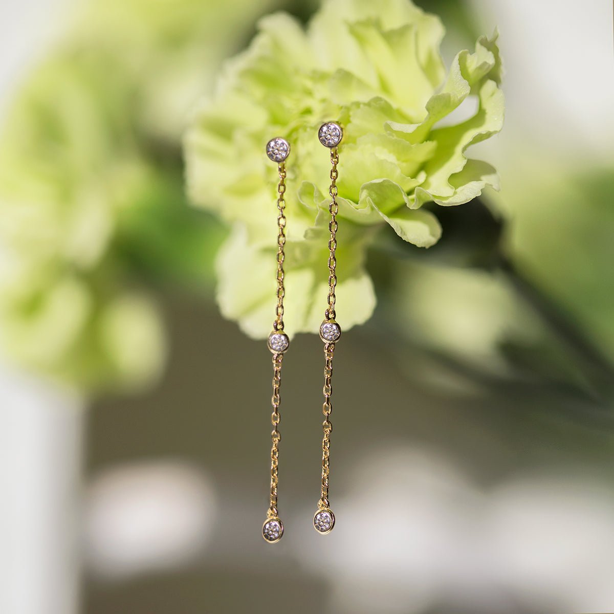Rose gold vermeil white zirconia drop earrings hanging in front of a soft green carnation