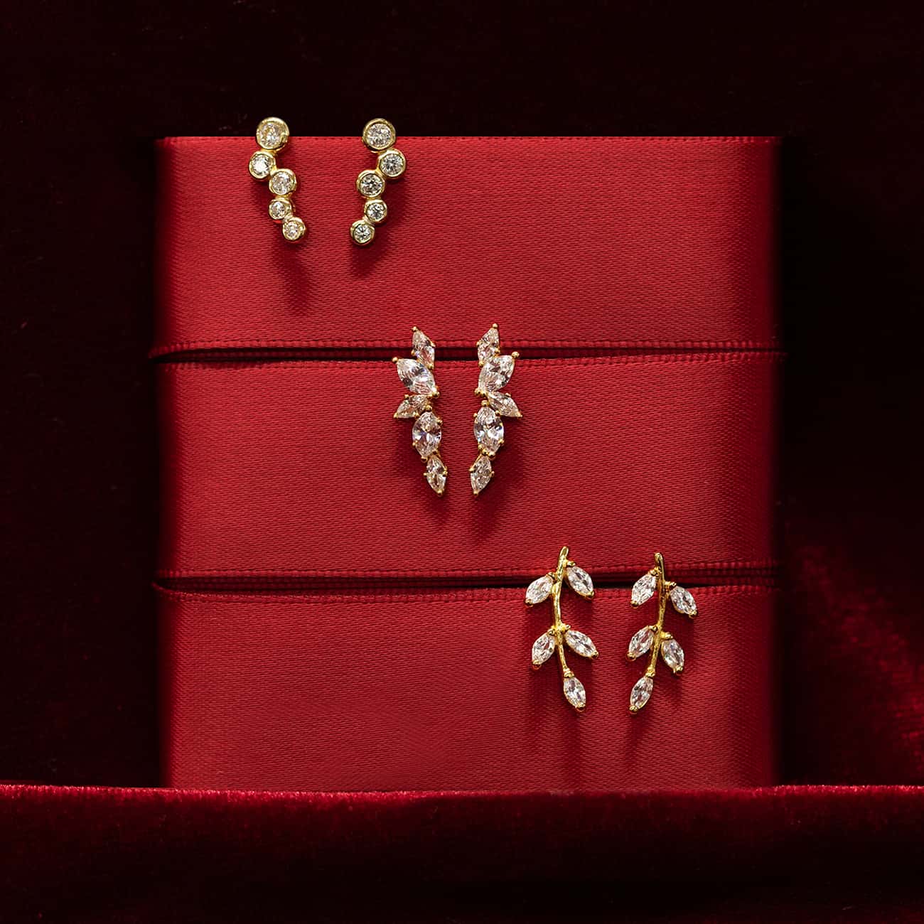 Three pairs of gold clear-stone stud earrings displayed on red ribbon