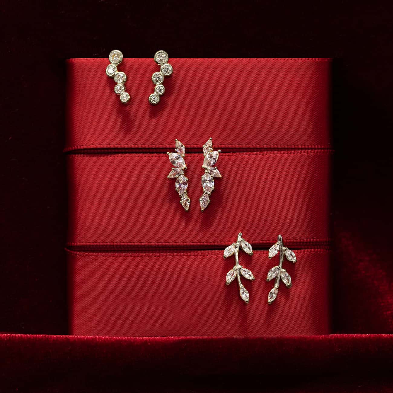 Three pairs of silver clear-stone stud earrings displayed on red ribbon