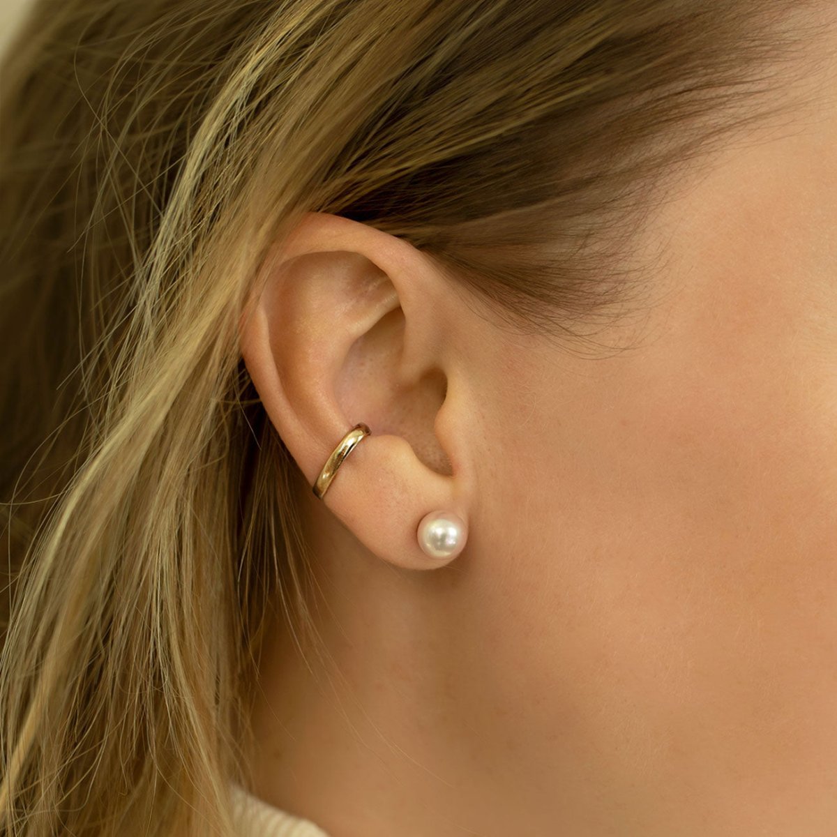 Sterling silver pearl stud shown on a model's lobe below a plain gold ear cuff