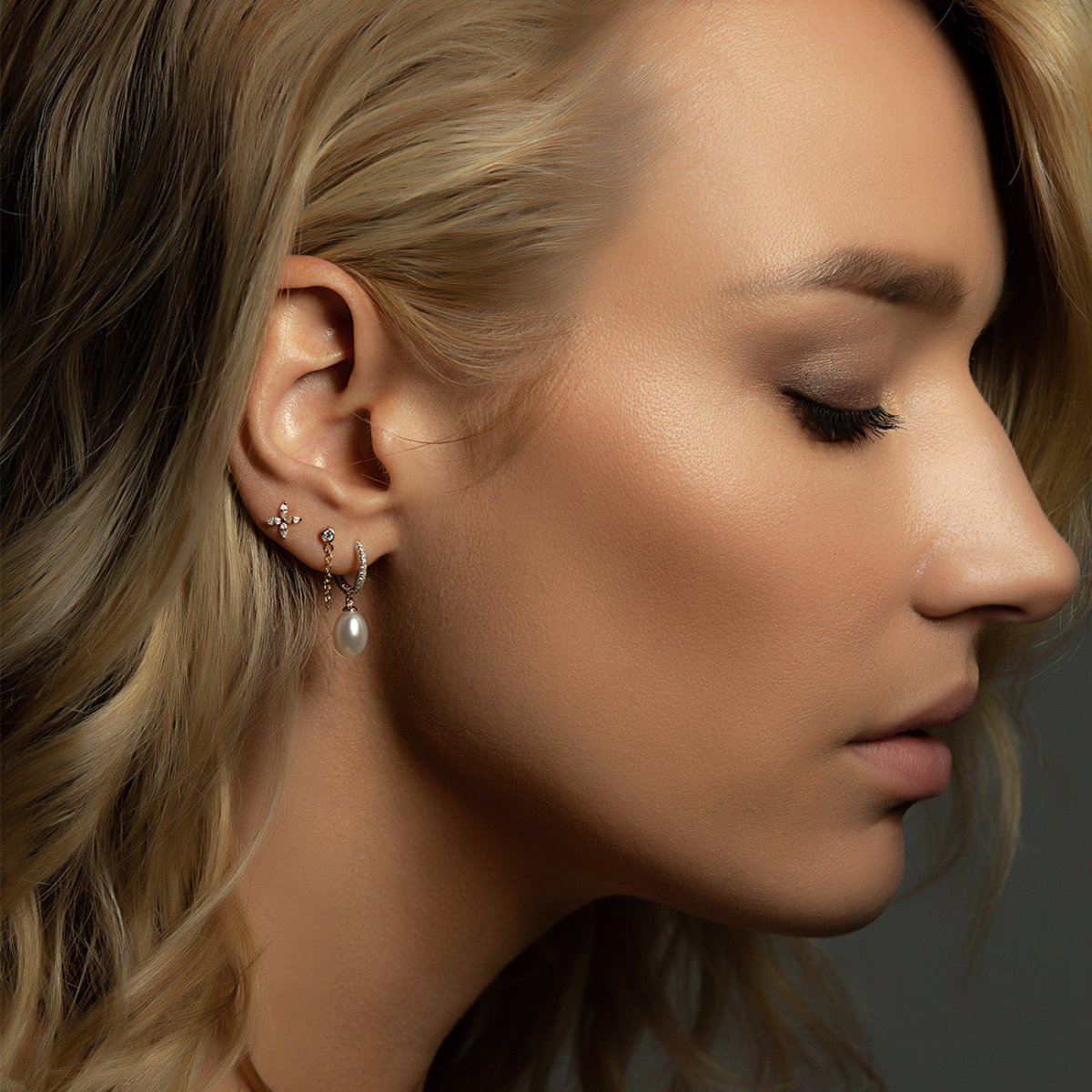 Sterling silver crystal flower stud shown with a pearl-drop hoop on a model's ear
