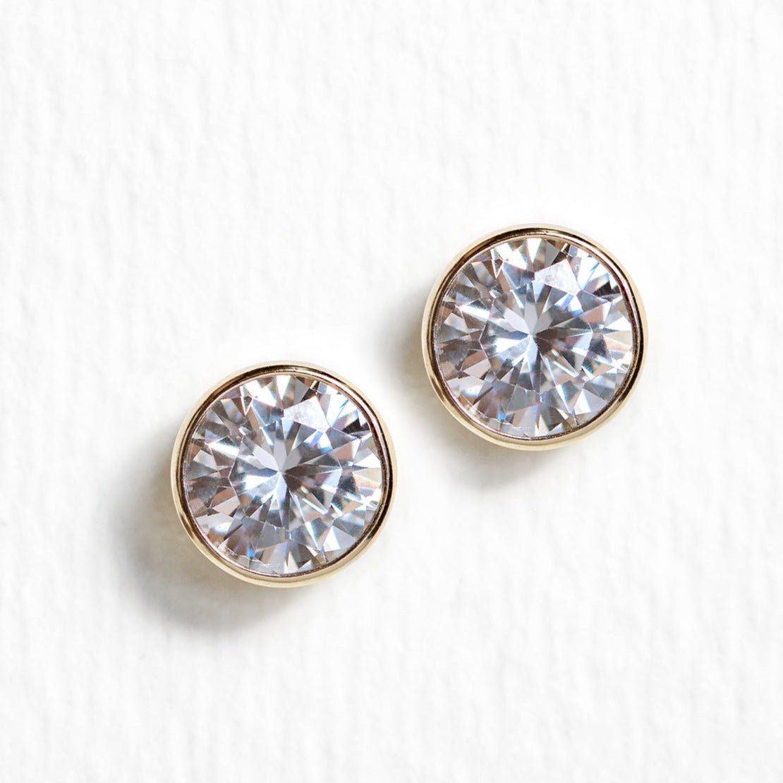 Gold vermeil white zirconia stud earrings, close-up detail on a cream textured surface