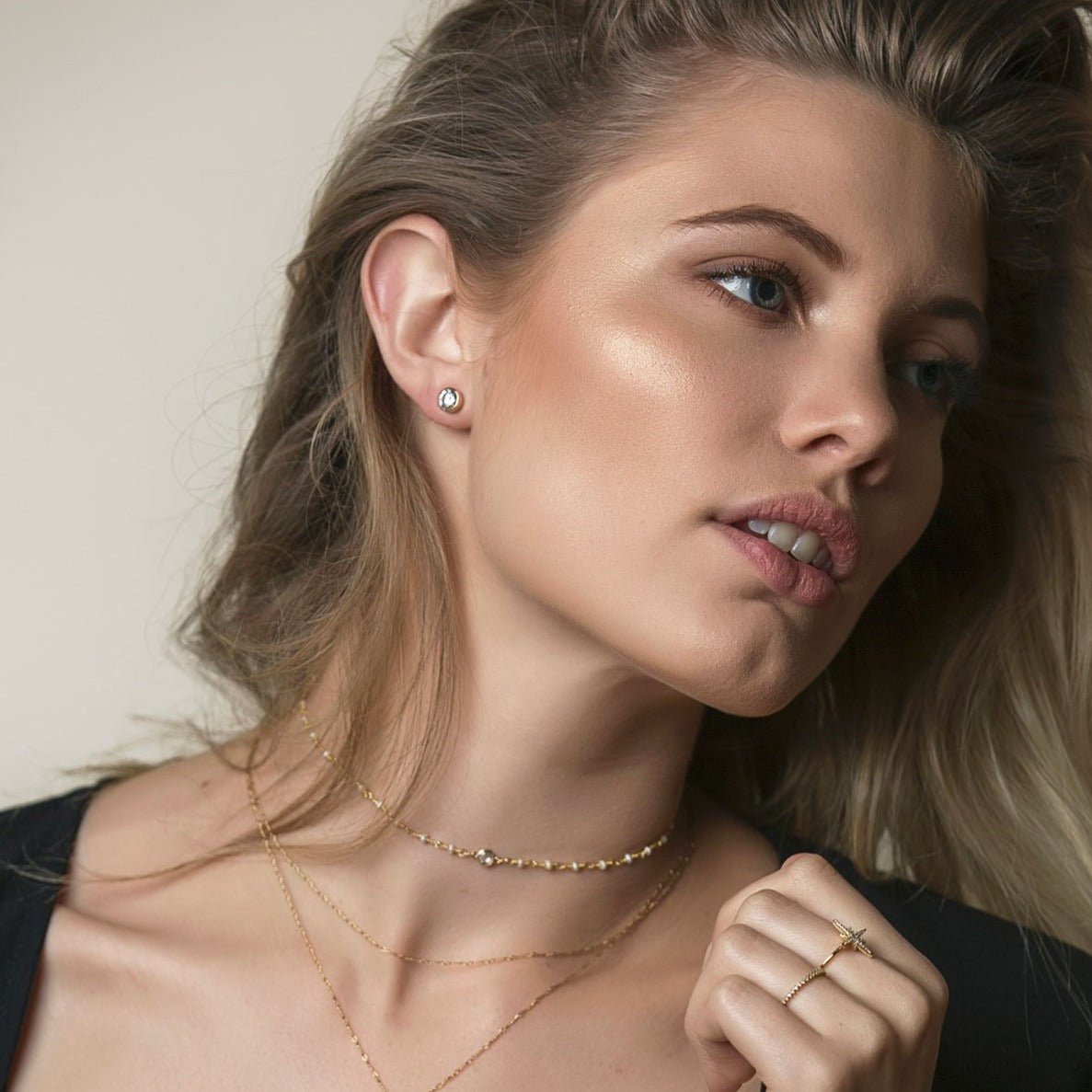Sterling silver white zirconia stud earring shown on a model's lobe with layered gold necklaces