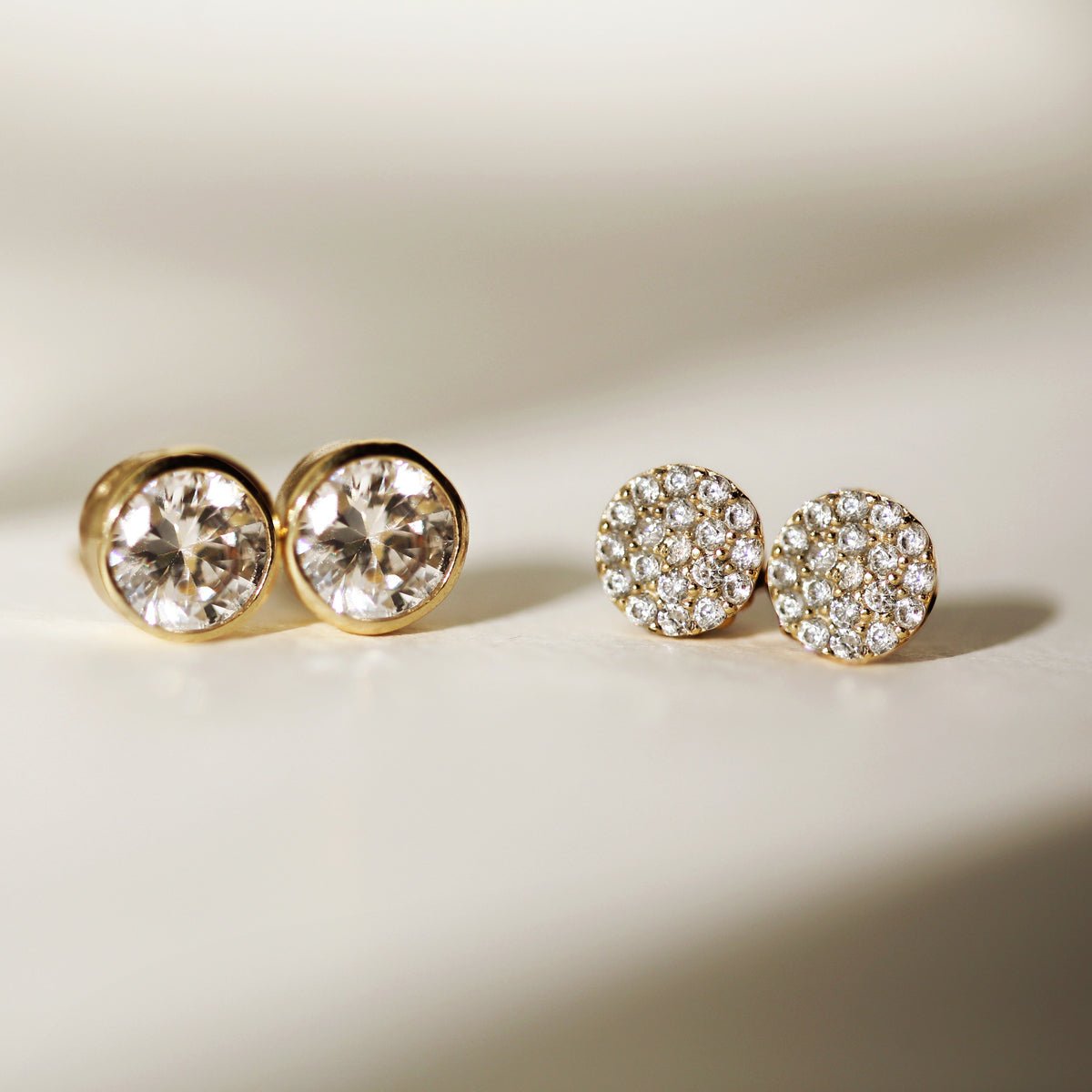 Gold vermeil pavé round studs with white zirconia beside solitaire studs, on a cream background