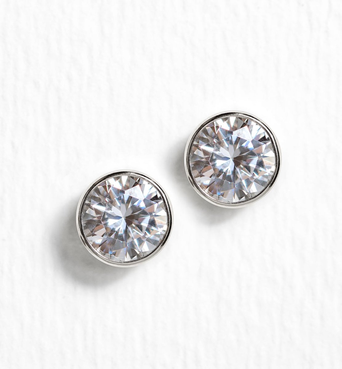 Sterling silver bezel-set stud earrings with round white zirconia stones, on a white background