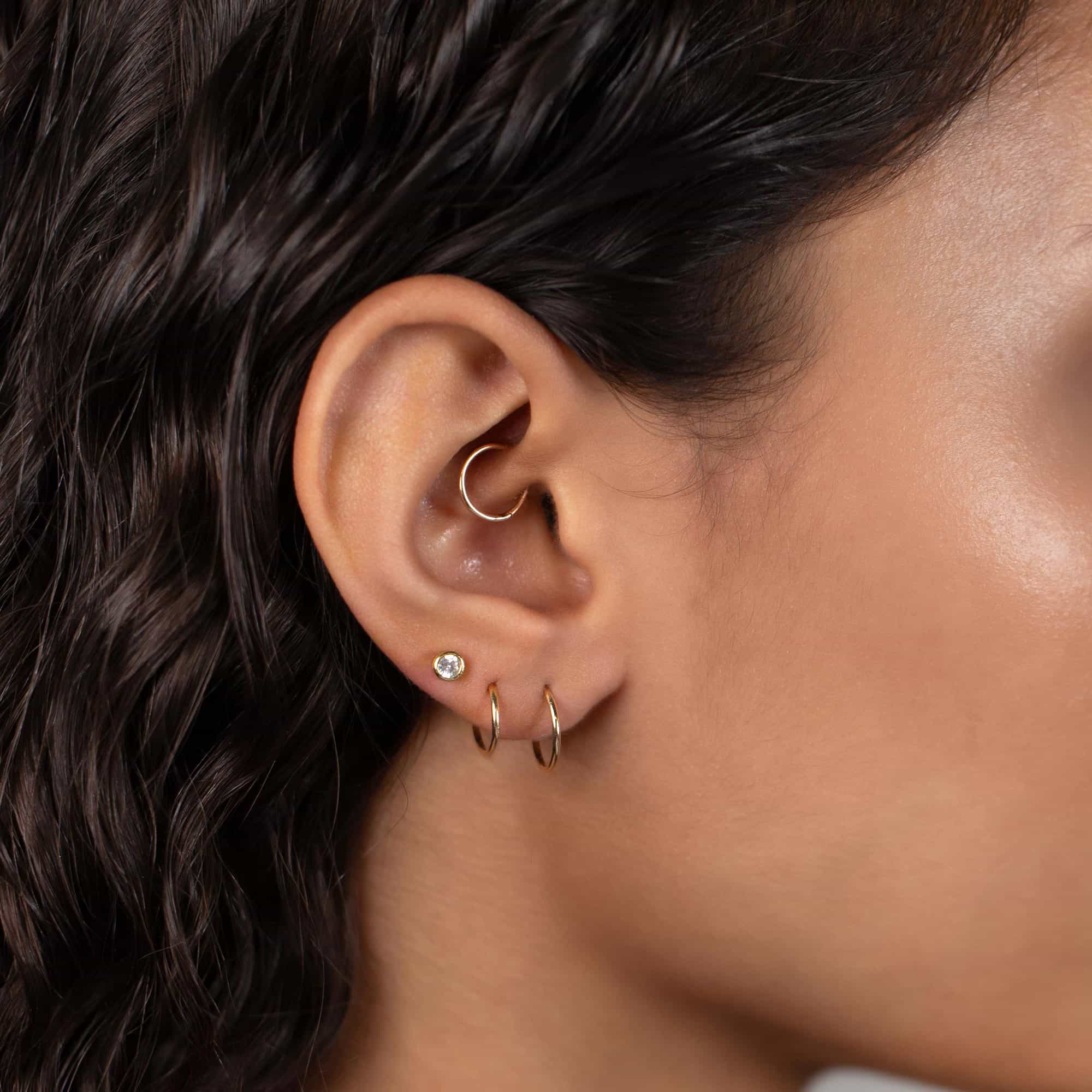 Gold-filled thin endless huggie hoops shown stacked on a model's lobe