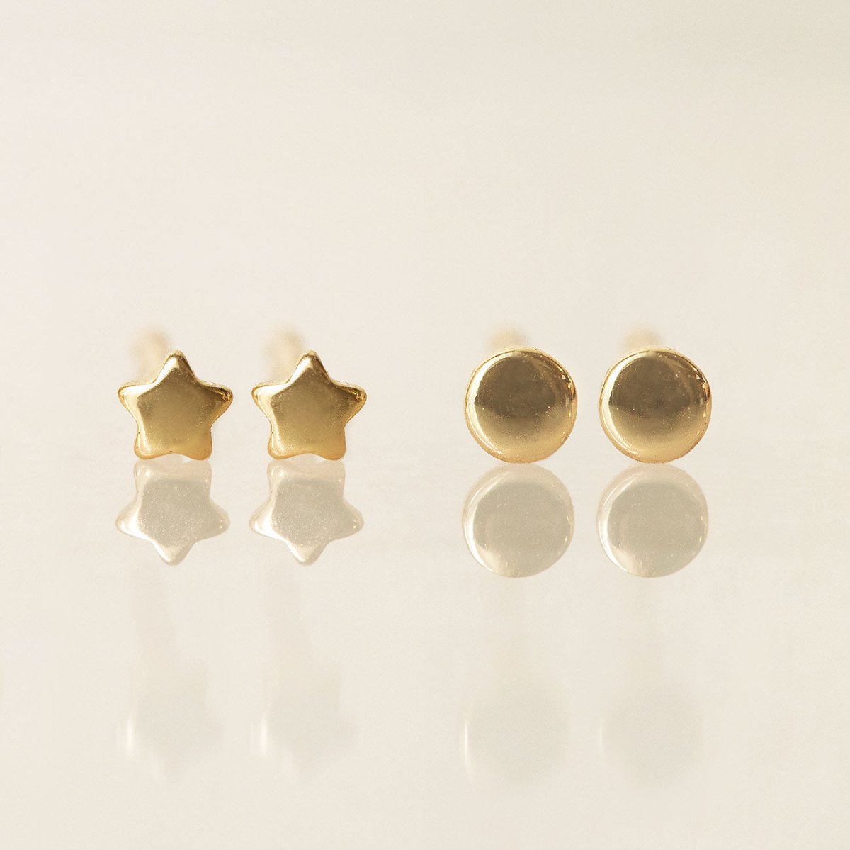 Gold vermeil tiny star studs and disc studs, close-up detail on a cream background