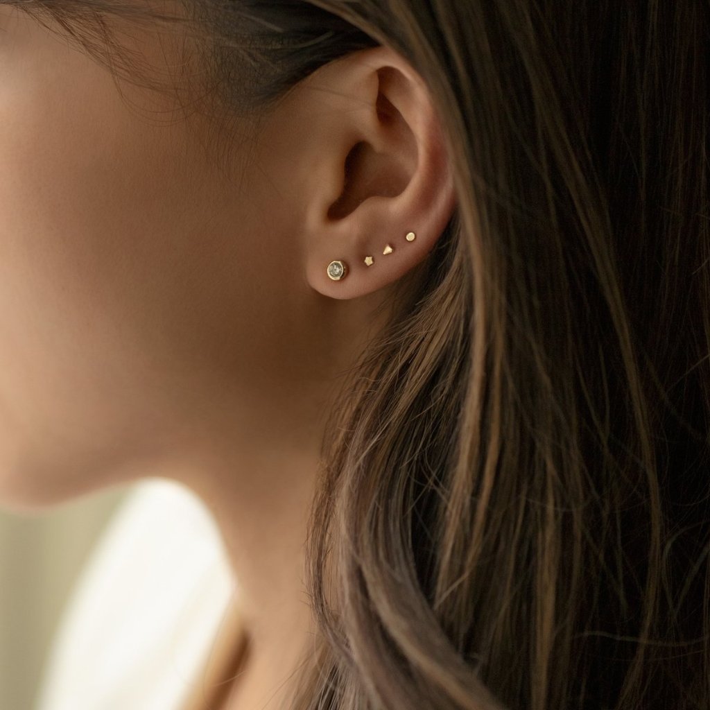 Gold vermeil tiny star, circle and bezel-set stone studs shown on a model's lobe