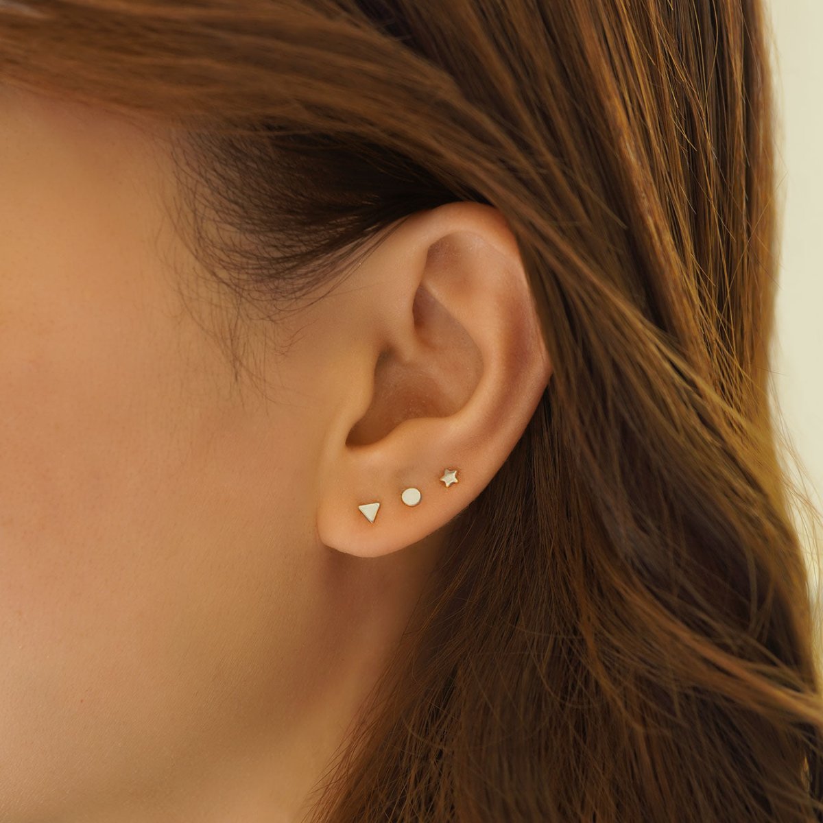 Sterling silver tiny triangle, circle and star studs shown on a model's lobe