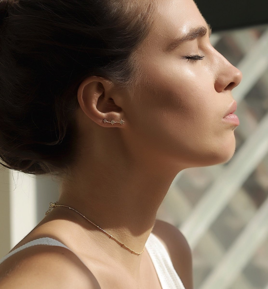 Sterling silver three-star ear climber with white zirconia, shown on a model's lobe in sunlight