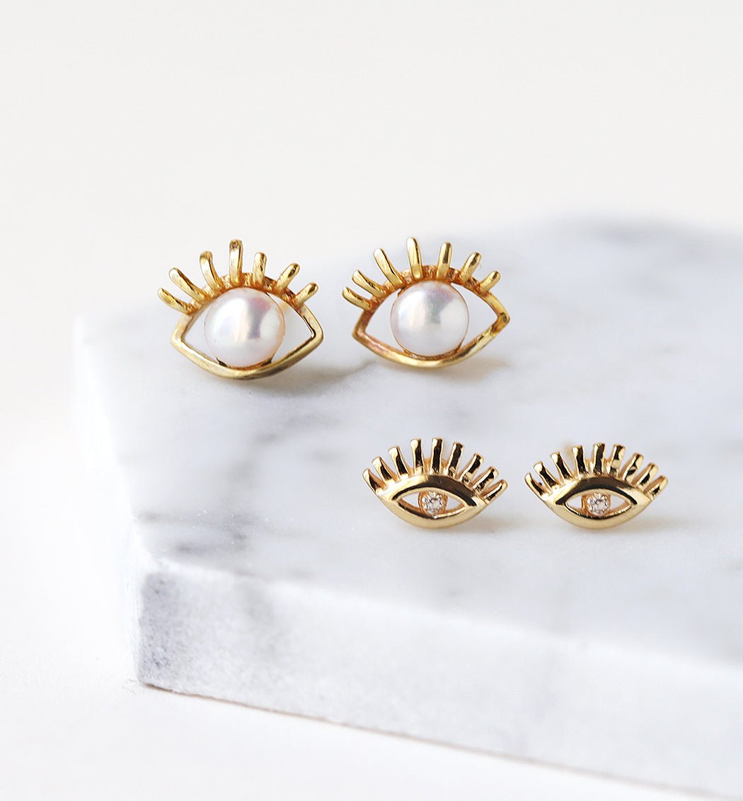 Gold vermeil evil eye studs with pearl and clear-stone versions, shown on white marble
