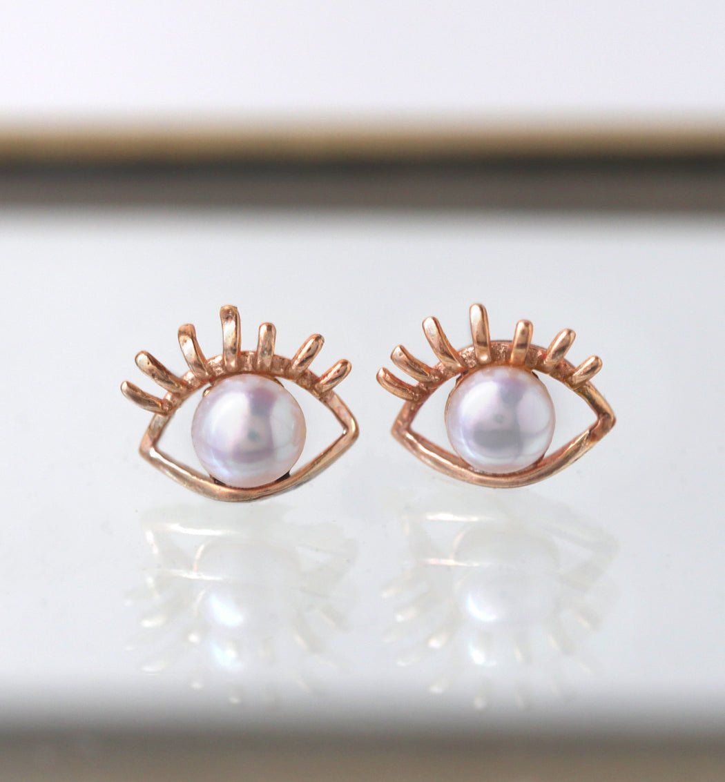 Rose gold vermeil evil eye stud earrings with white pearl centers, on a cream tray
