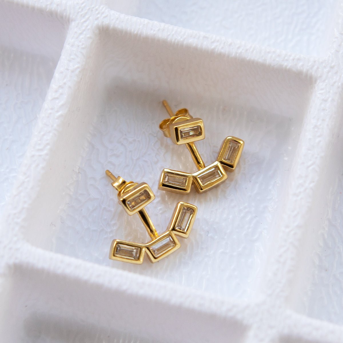Gold vermeil baguette ear jacket earrings with clear stones curving below the lobe, on a white background
