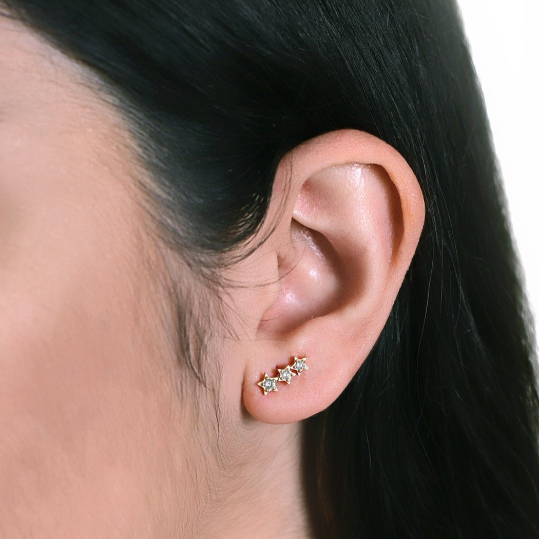 Gold vermeil three-star climber studs with clear stones, shown on a model's lobe