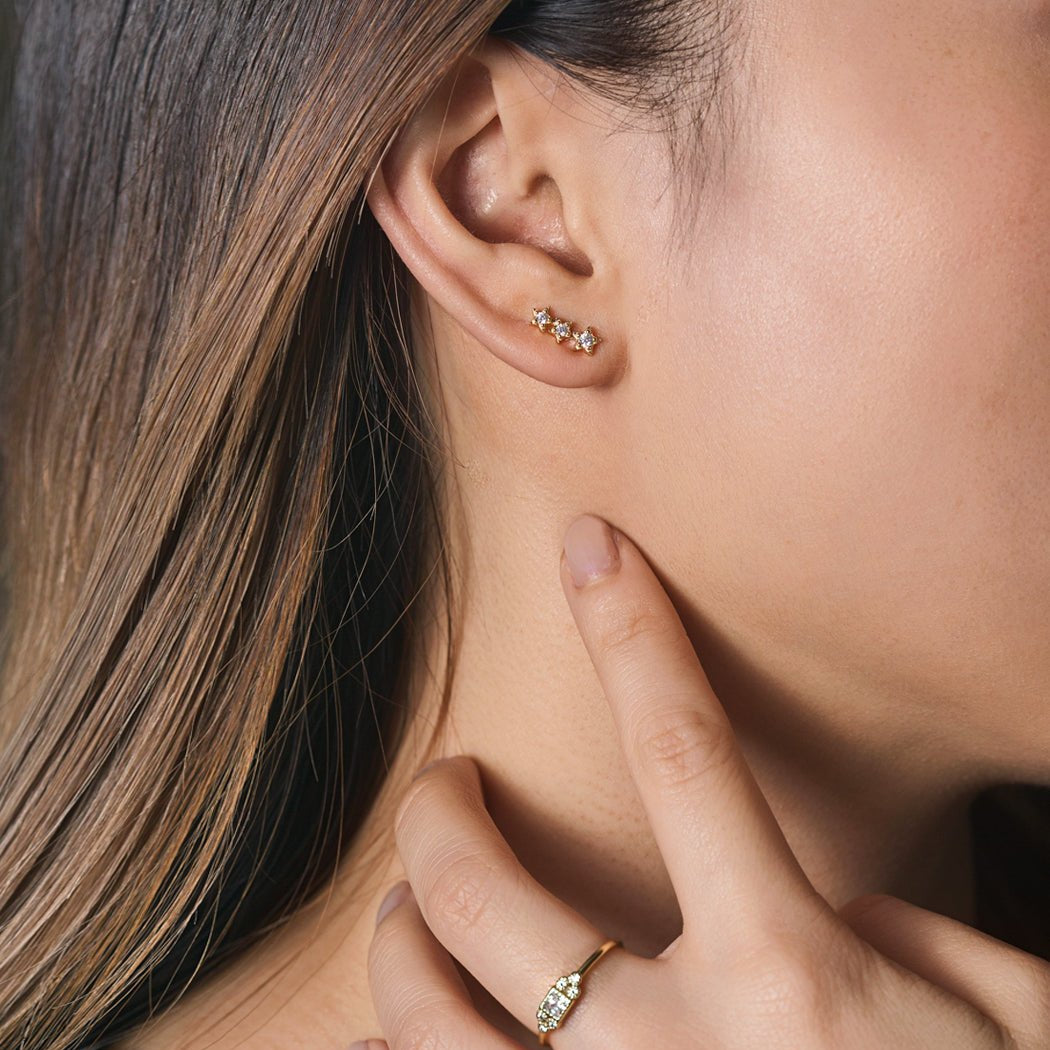 Sterling silver three-star dainty studs with clear stones, shown on a model's upper lobe