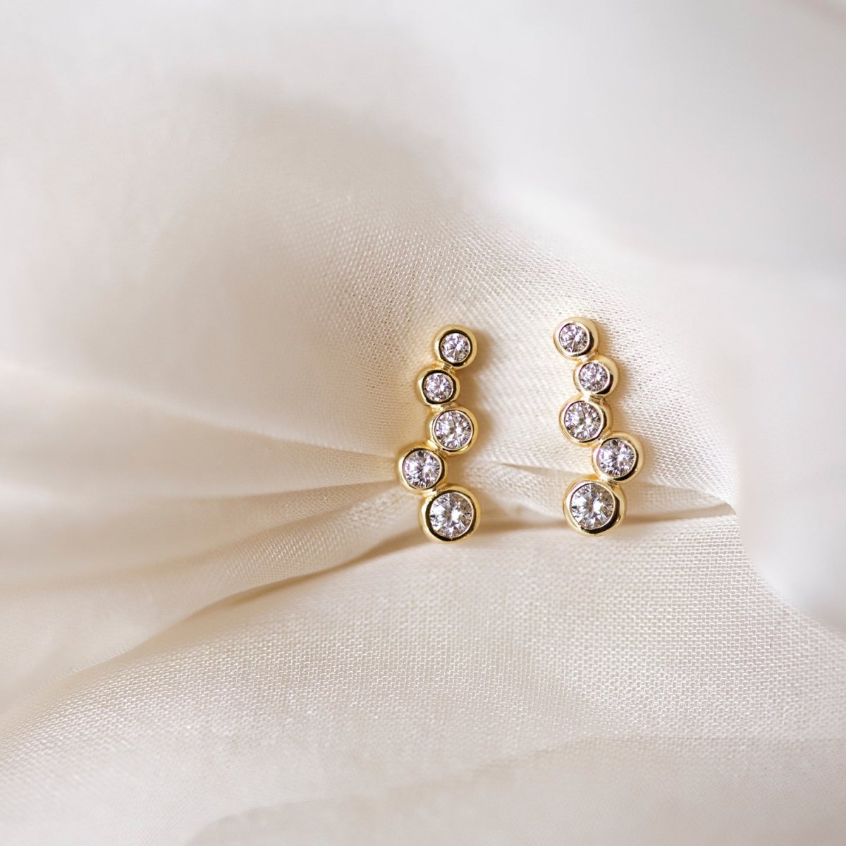 Pair of gold vermeil bezel-set ear climbers with five graduated clear crystals, on cream fabric