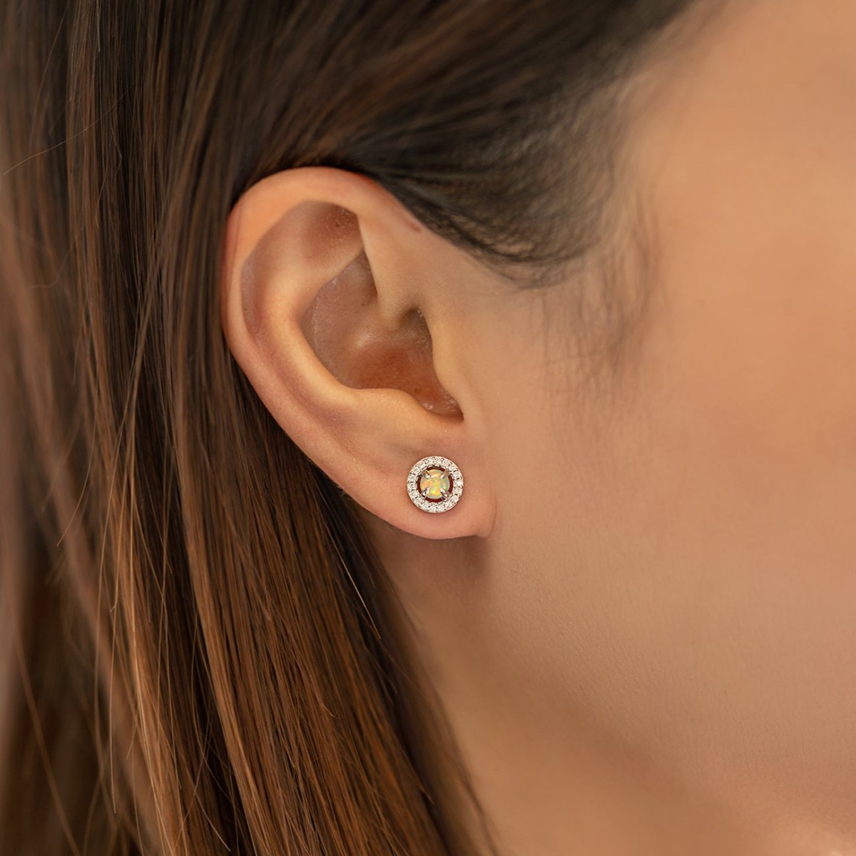 Sterling silver opal halo stud with a clear pavé surround, shown on a model's lobe