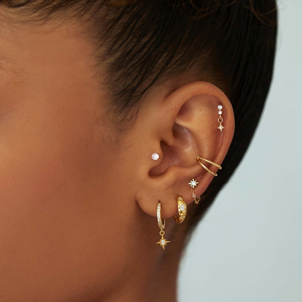 Gold ear stack on a model with star-drop huggies, a twisted ear cuff and clear-stone studs across several piercings