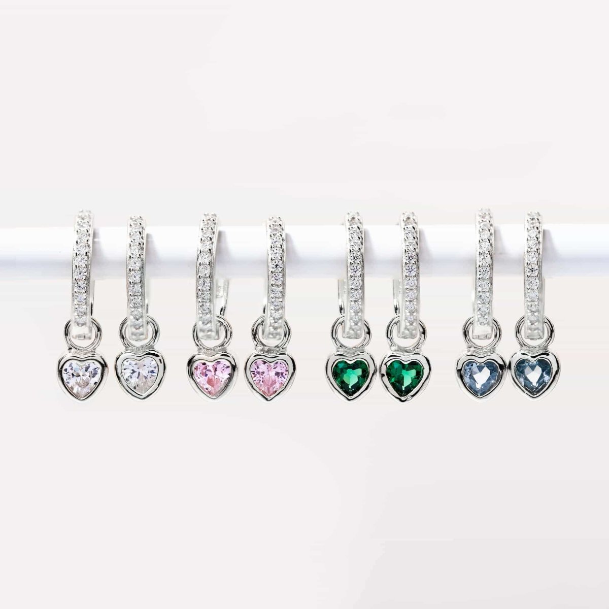 Sterling silver pavé huggie hoops with heart charms in clear, pink, green and blue stones, in a row