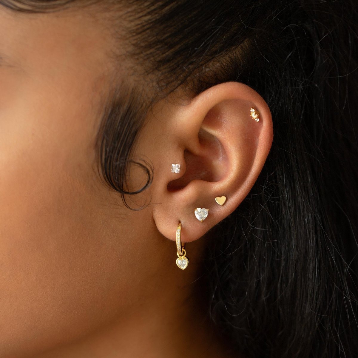 Gold vermeil heart stud with a clear white zirconia stone shown on a model's lobe in an ear stack