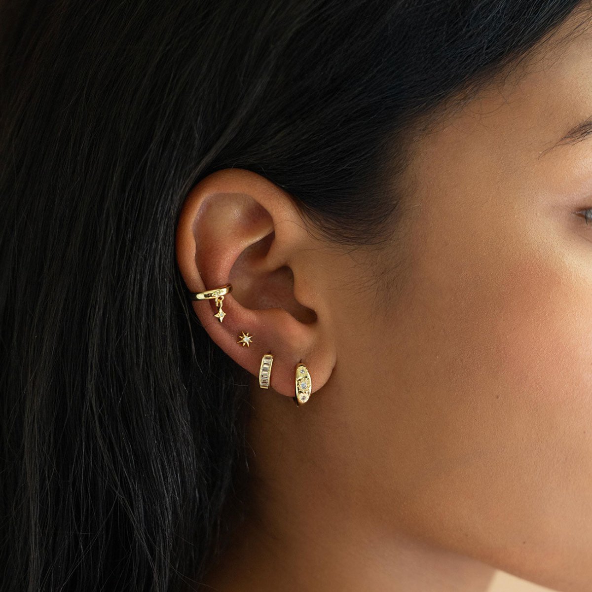 Gold ear stack on a model with a star ear cuff, baguette huggie and clear-stone studs across several piercings