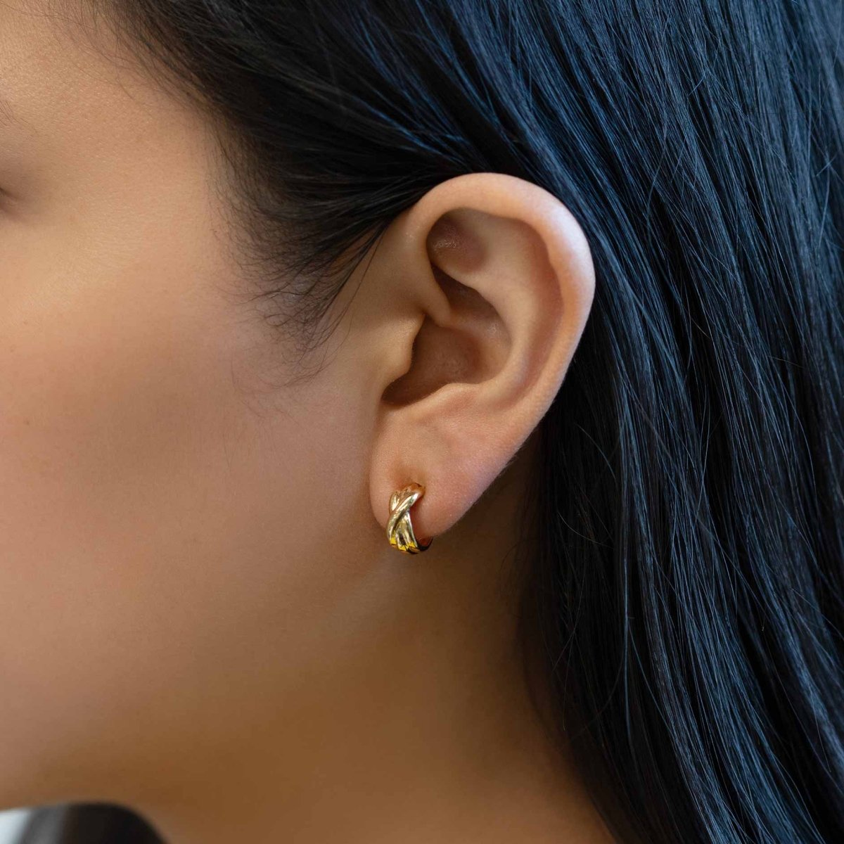 Gold vermeil twisted criss-cross huggie hoop shown on a model's lobe