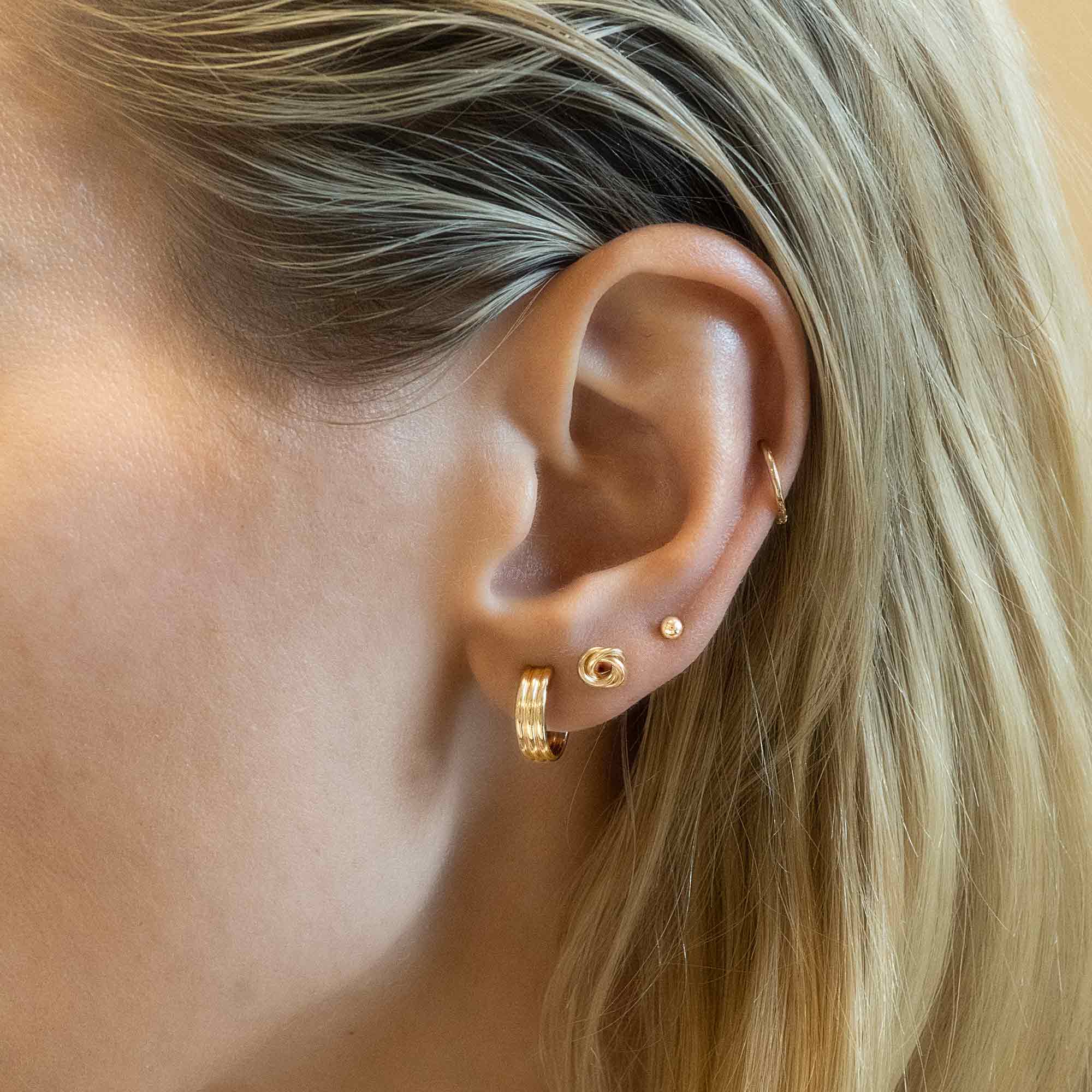 Gold-filled triple-ridge hoop shown on a model's lobe with smaller stud earrings