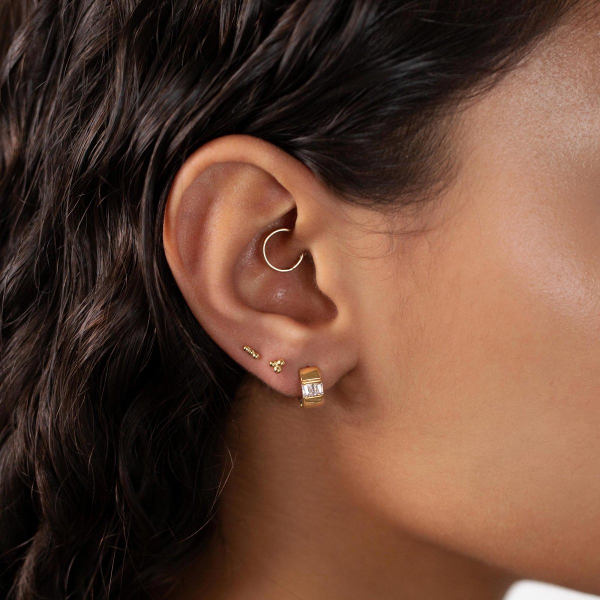 Gold vermeil tiny ball cluster studs shown on a model's lobe with a daith ring and huggie