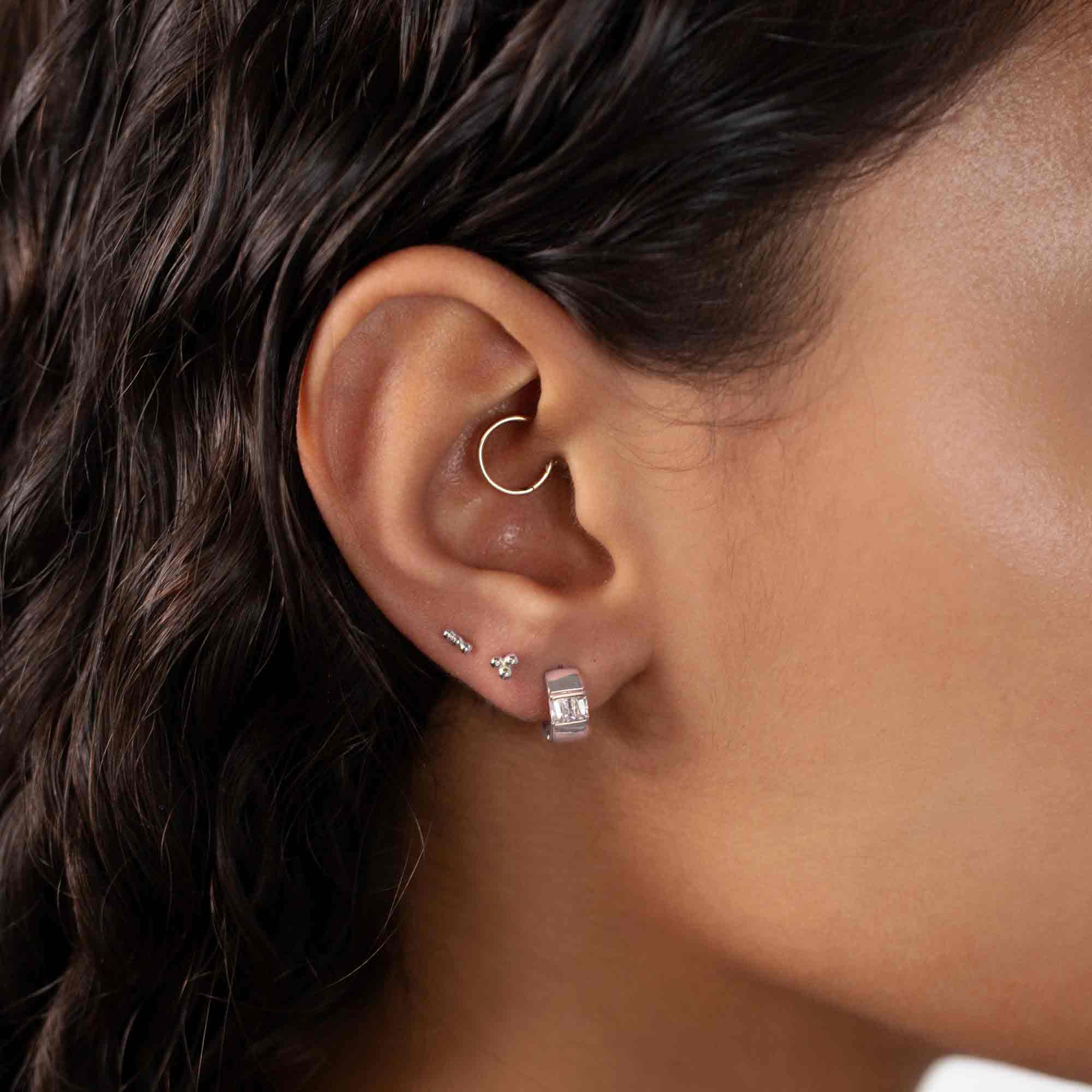 Sterling silver baguette huggie hoop with white zirconia, worn in a lobe piercing on a model's ear