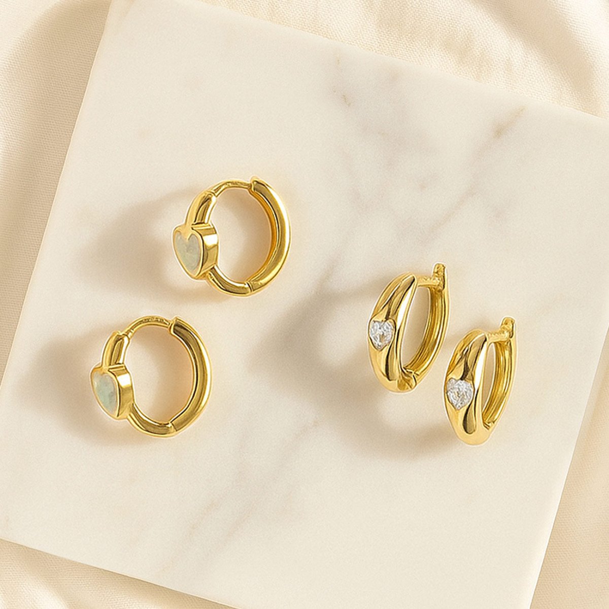 Gold vermeil heart inlay huggie hoops with white and clear stone hearts, on cream marble