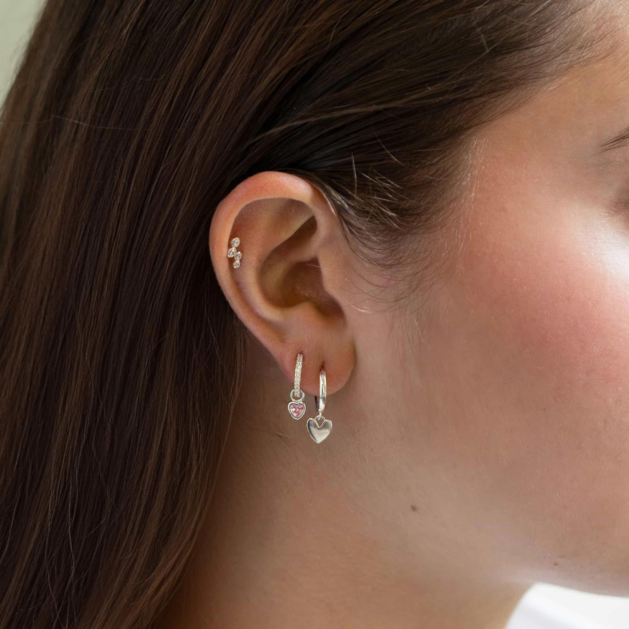 Sterling silver pavé huggie hoop with a pink heart charm, shown on a model's ear