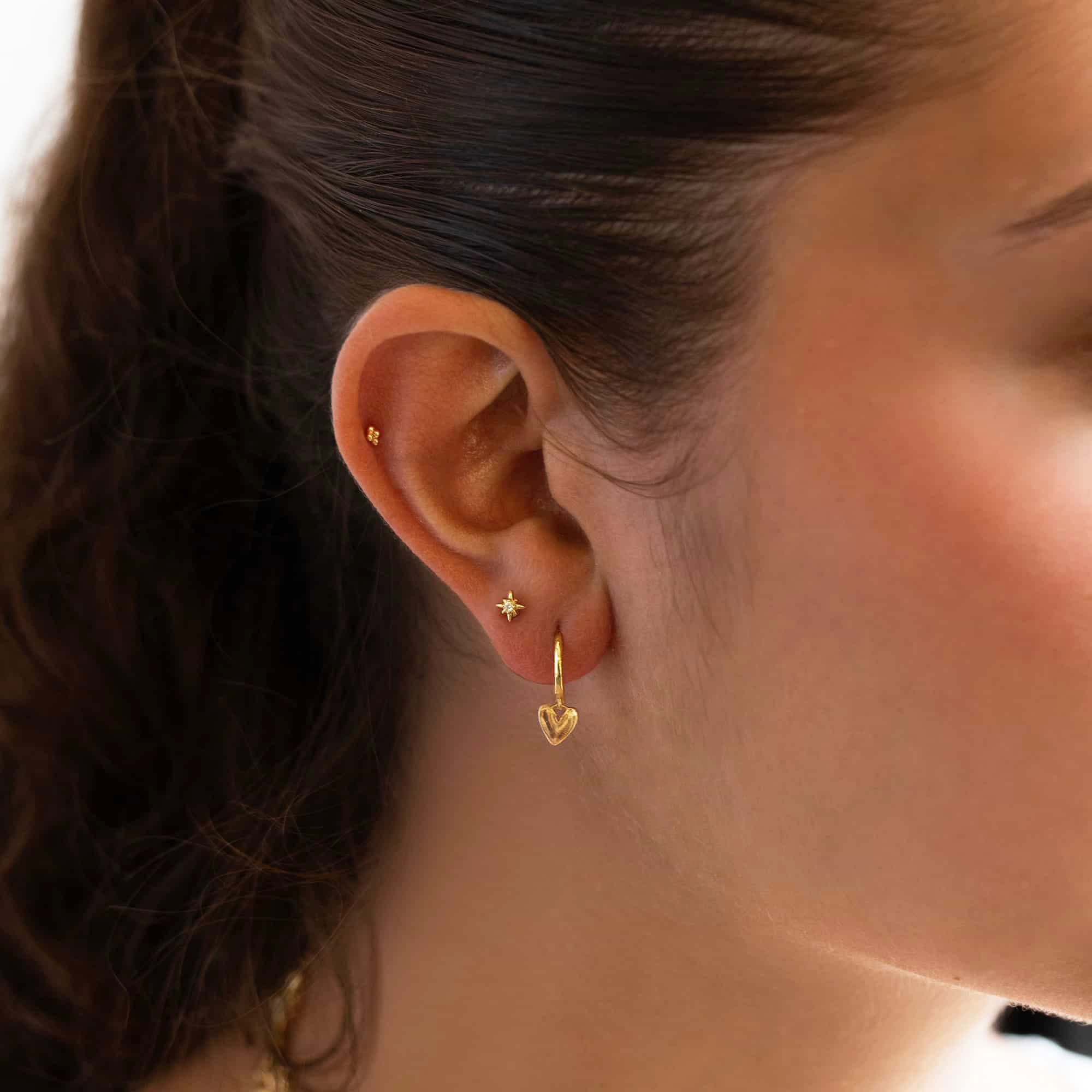 14K gold huggie hoop with a small heart charm, shown on a model's lobe and helix