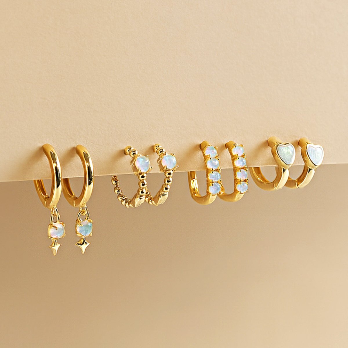 Assortment of gold opal huggie hoops in drop, beaded, and heart styles on a cream background