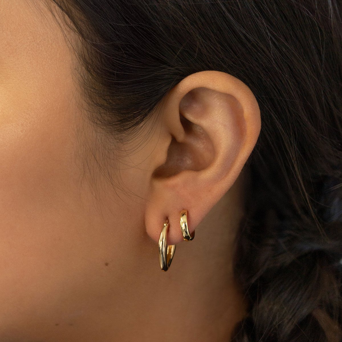 Gold vermeil mini huggie hoops shown stacked on a model's lobe