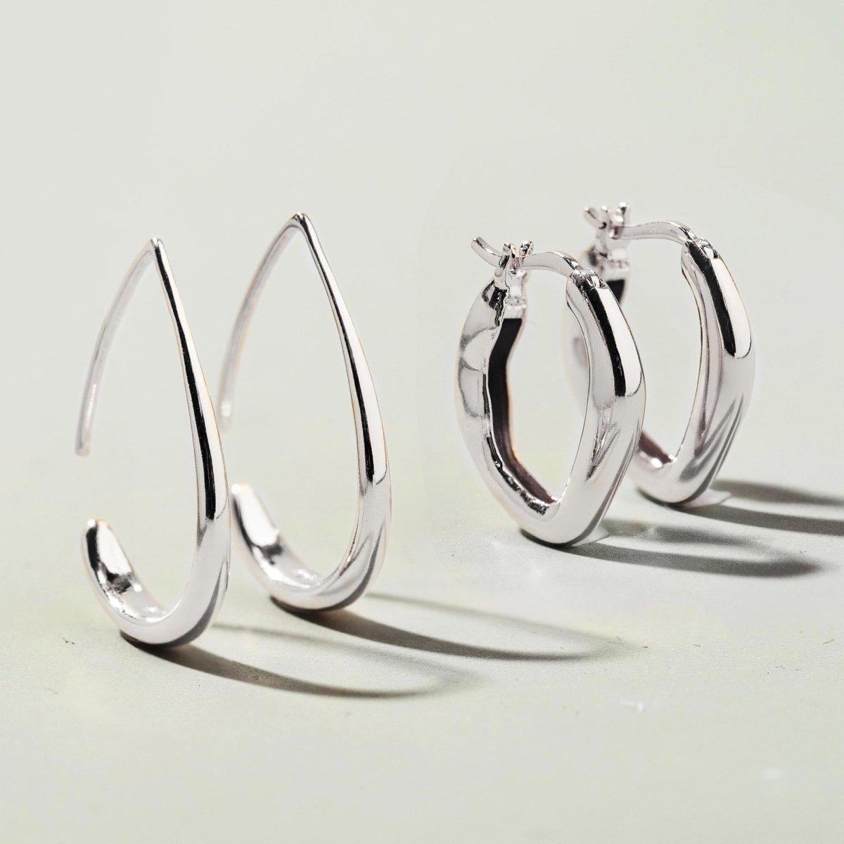 Sterling silver teardrop hoop earrings, front and clasp views shown together on a pale surface