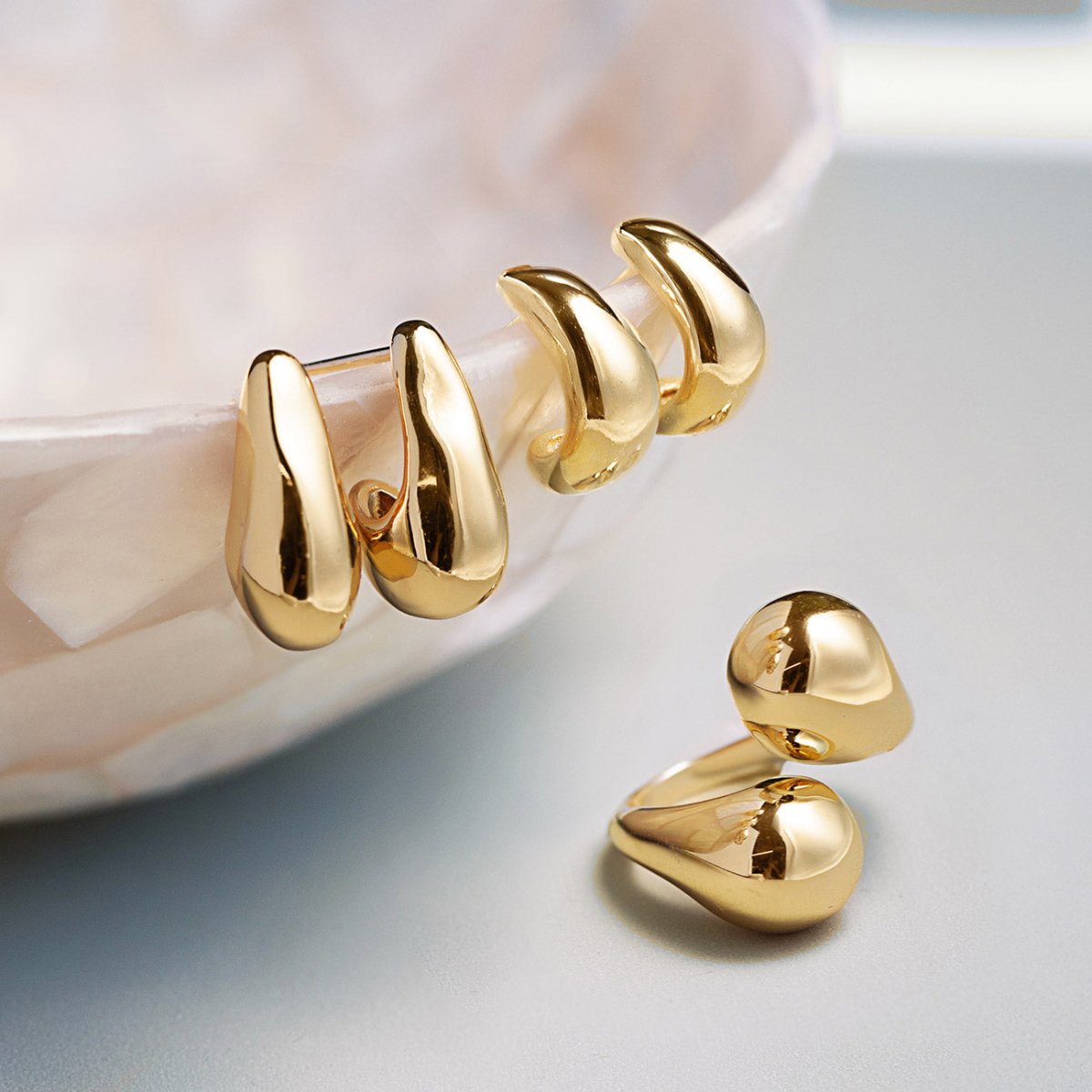 Gold hoop earrings on a light gray surface with a pearl dish - shop bold sculptural jewelry