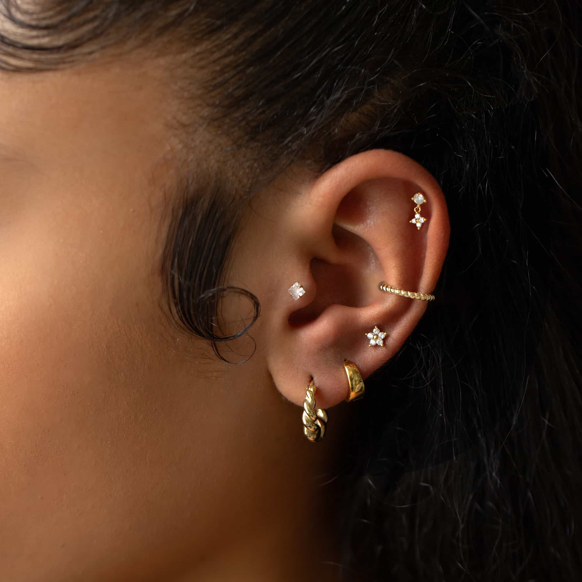 14K gold flower flat back studs with clear white zirconia shown on a model's lobe and helix