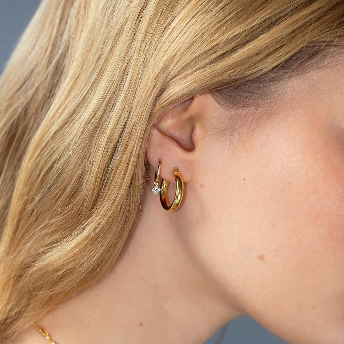 Gold vermeil Flor huggie hoop with a white zirconia charm, paired with a thick hoop on a model's lobe