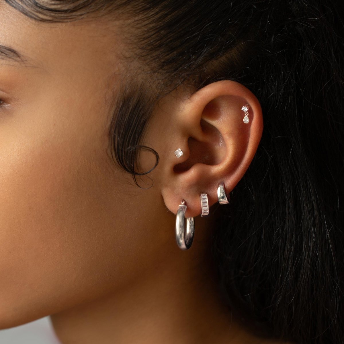 Sterling silver baguette huggie hoop with clear stones, styled in a model's ear stack