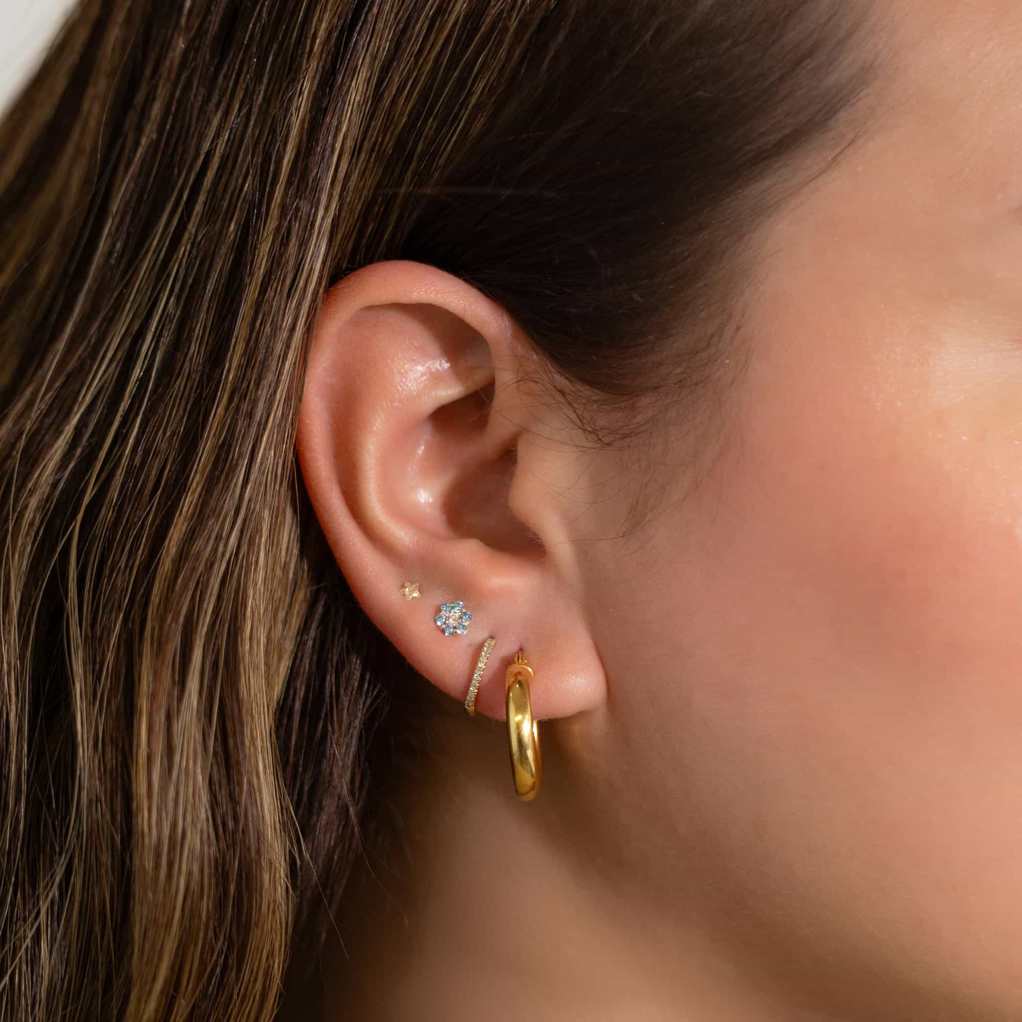 14K gold aquamarine flower cluster stud shown on a model's lobe beside a clear flower stud
