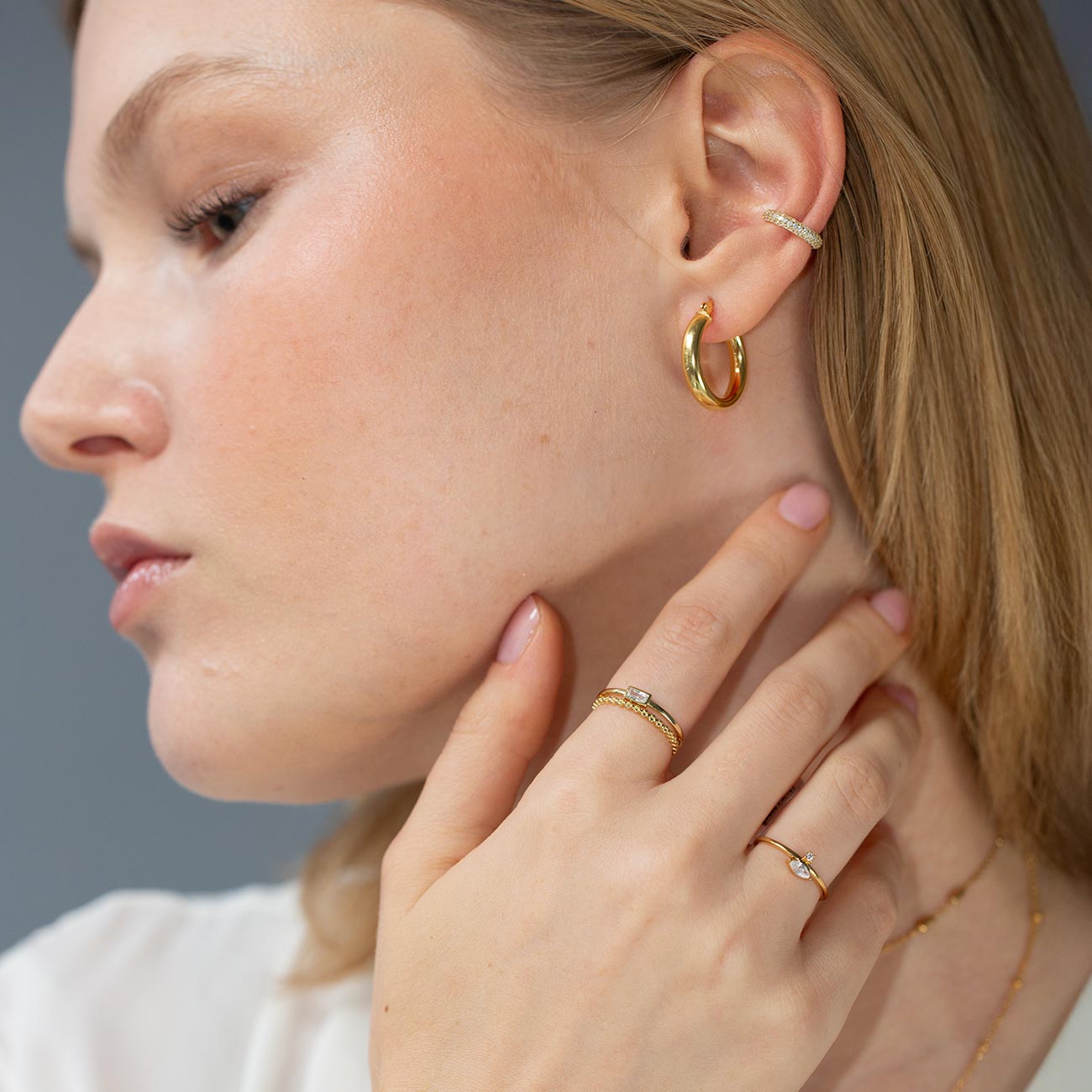 Gold marquise band ring with a clear stone shown on a model's hand near her neck