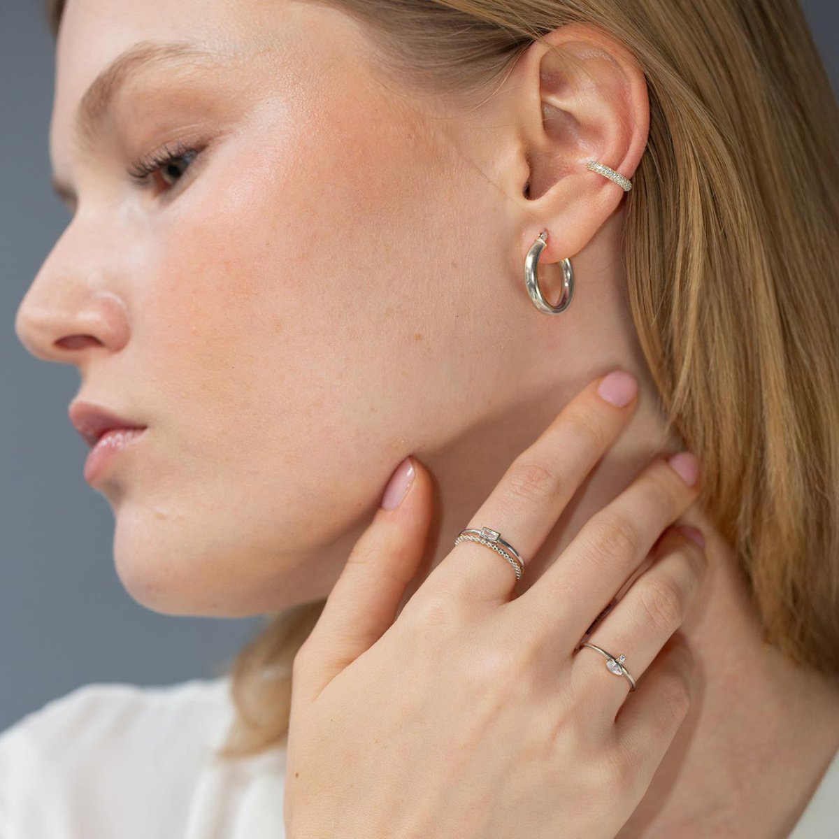 Silver marquise band ring with a clear stone shown stacked on a model's finger