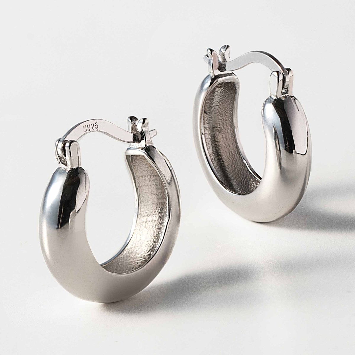 Sterling silver small thick domed hoop earrings, close-up on a white background