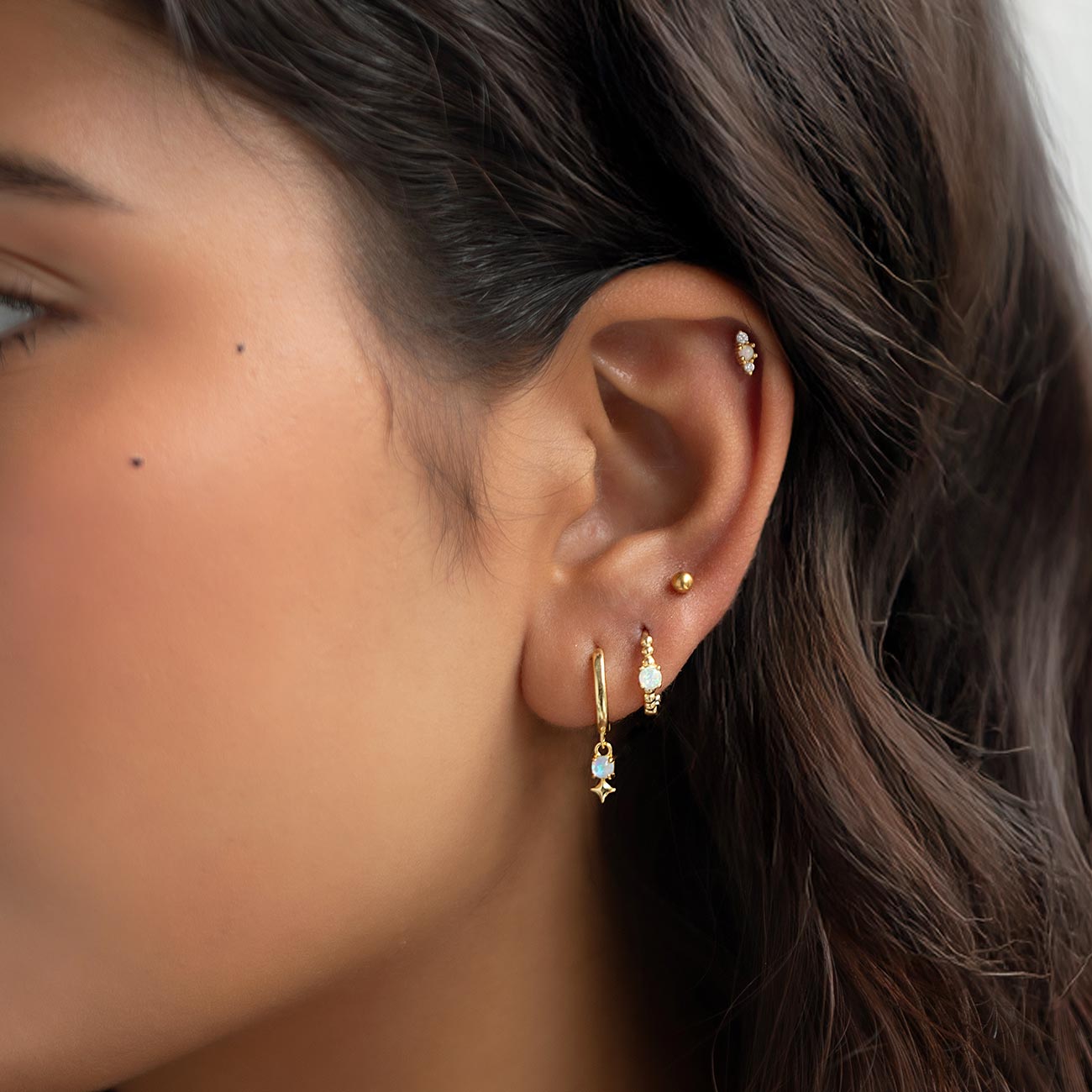 Gold opal drop huggie, beaded huggie, and gold ball stud styled on a model's ear
