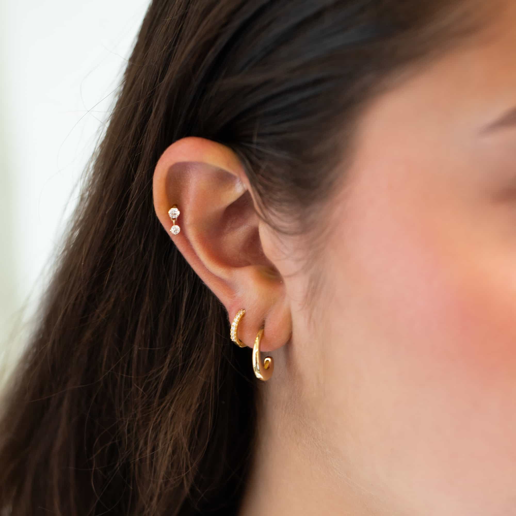 Gold clear-stone studs and plain and pavé huggie hoops shown in an ear stack on a model