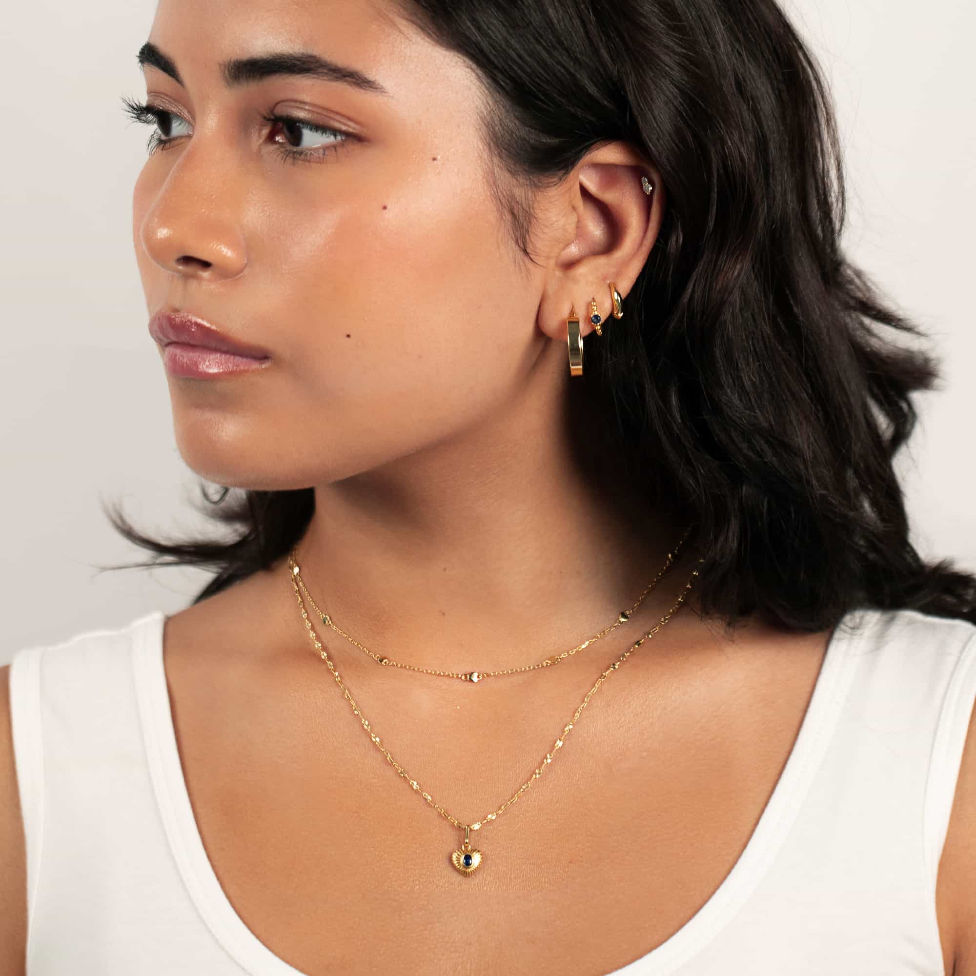 Gold vermeil ridged heart charm necklace with an oval blue sapphire, shown on a model's neckline