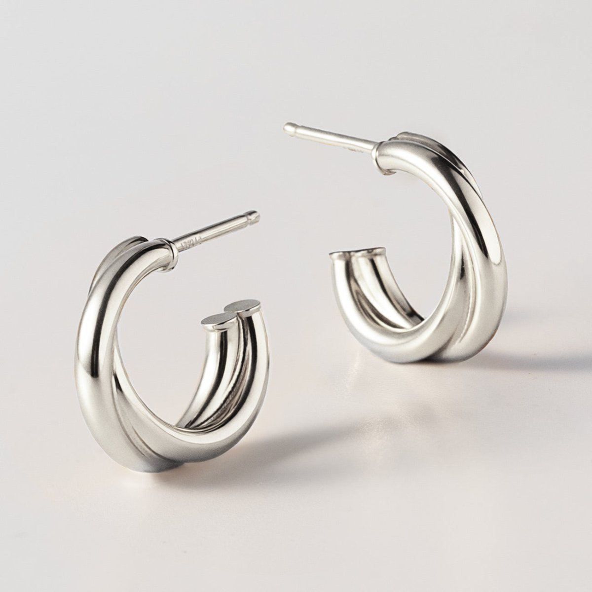 Sterling silver criss cross mini hoops, close-up detail of the crossover bands on a white background